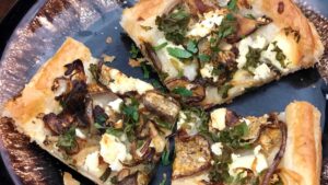 Small pieces of flatbread with eggplant slices, onion slices, small leafy greens and small cheese crumbles