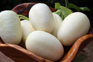 A wooden bowl with white, egg-shaped 'Dragon's Egg' cucumbers