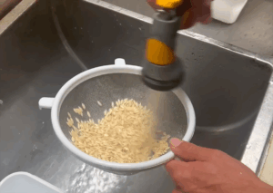 A person uses a sink sprayer to rinse cucumber seeds in a colander.
