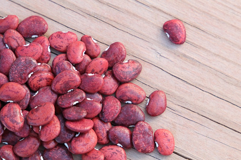 A pile of red speckled lima beans on a wood surface