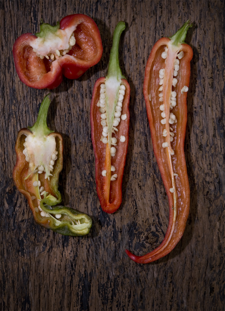 Four different peppers sliced vertically in half, showing the interior ribbing and seeds