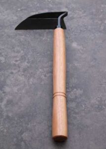 A hand hoe with a forged blade and wooden handle on a smooth rock surface