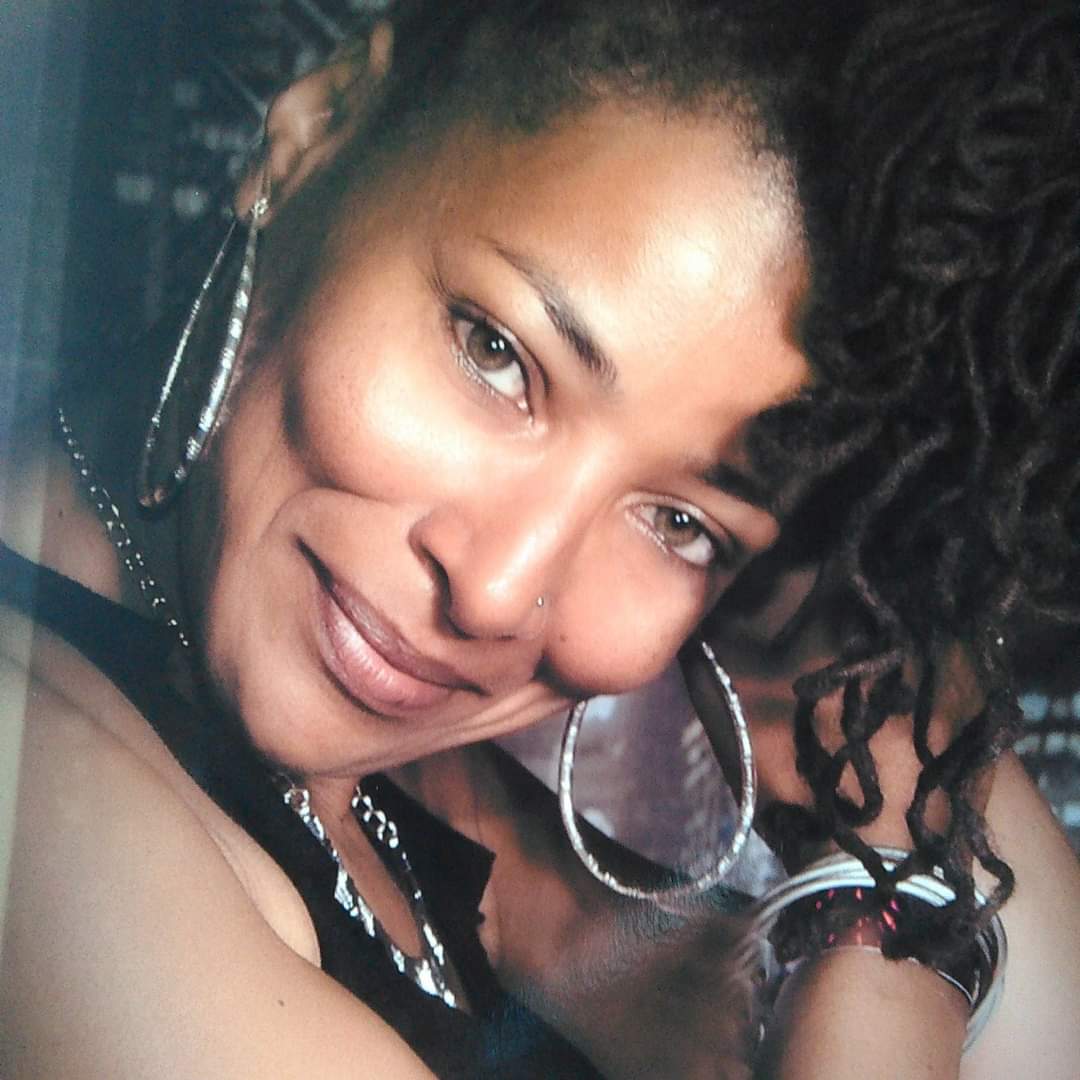 A woman with large hoop earrings smiles to camera.