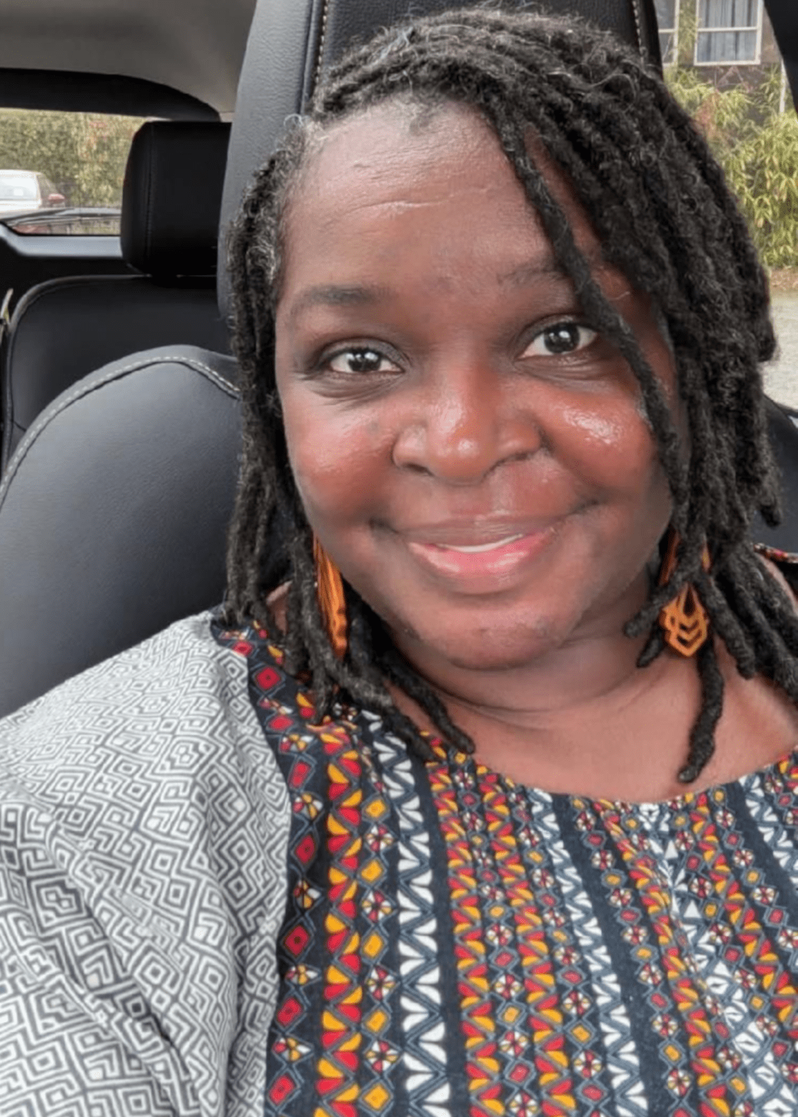 A woman in a car smiles to camera.