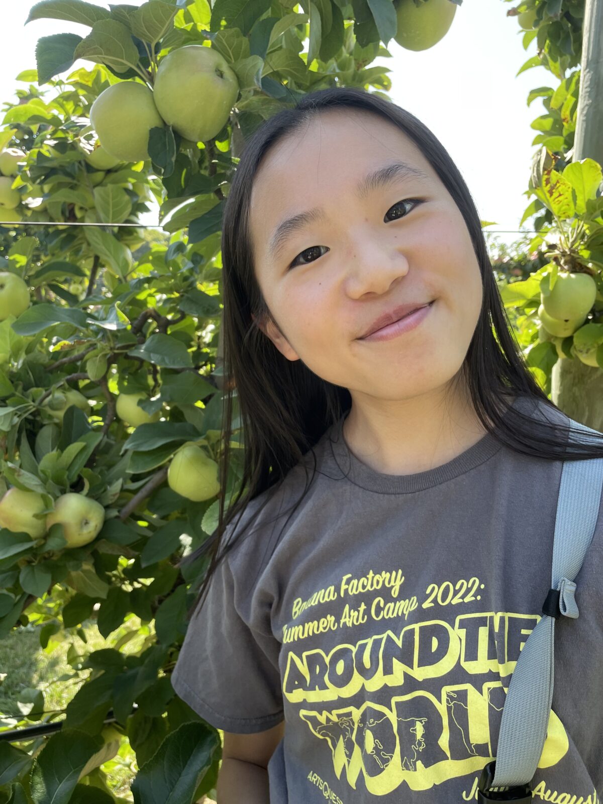A woman smiles to camera in front of an apple tree.