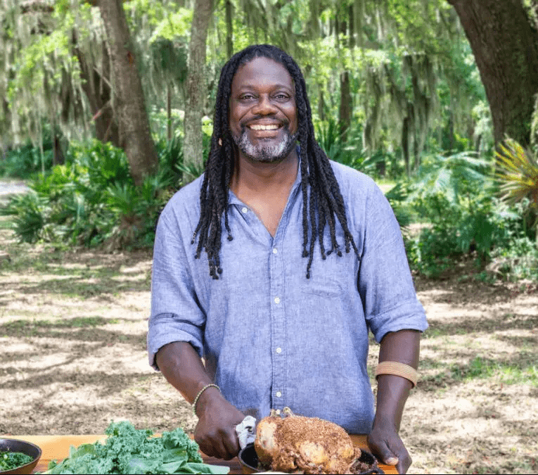 A man holding a roast chicken on a table.