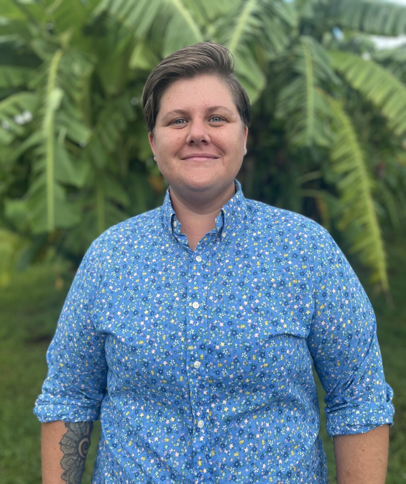 A woman, standing in front of a palm plant, smiles to camera.
