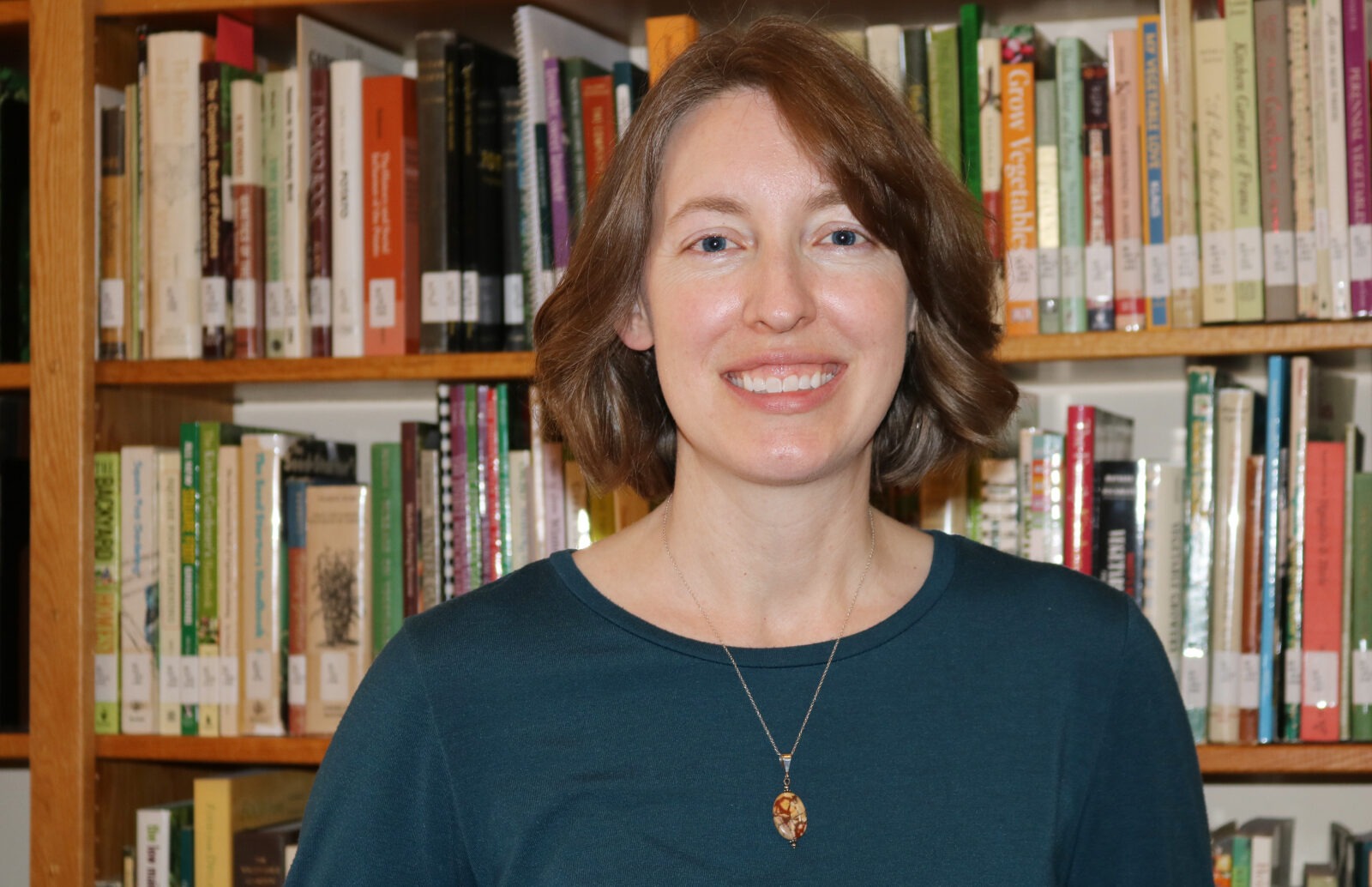 A woman smiles to camera in front of book lined shelves.