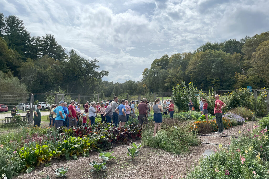 A crowd gathers in a garden where a lecture is being given.