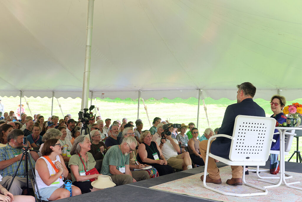 A crowd looks at two people on a stage sitting in white chairs.