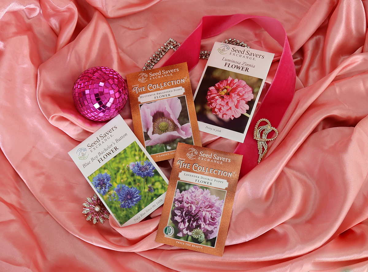 Four seed packets of various flowers arranged on a pink silk cloth with a pink disco ball and other trinkets